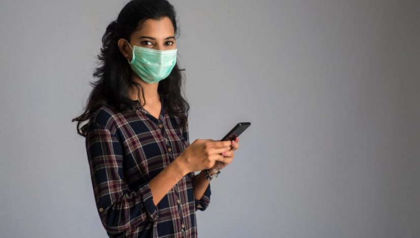 Woman with a surgical mask using a smartphone for communication. work from home concept.