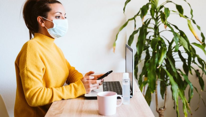 young woman working on laptop at home, wearing protective mask. work from home, stay safe during coronavirus covid-2019 concpt